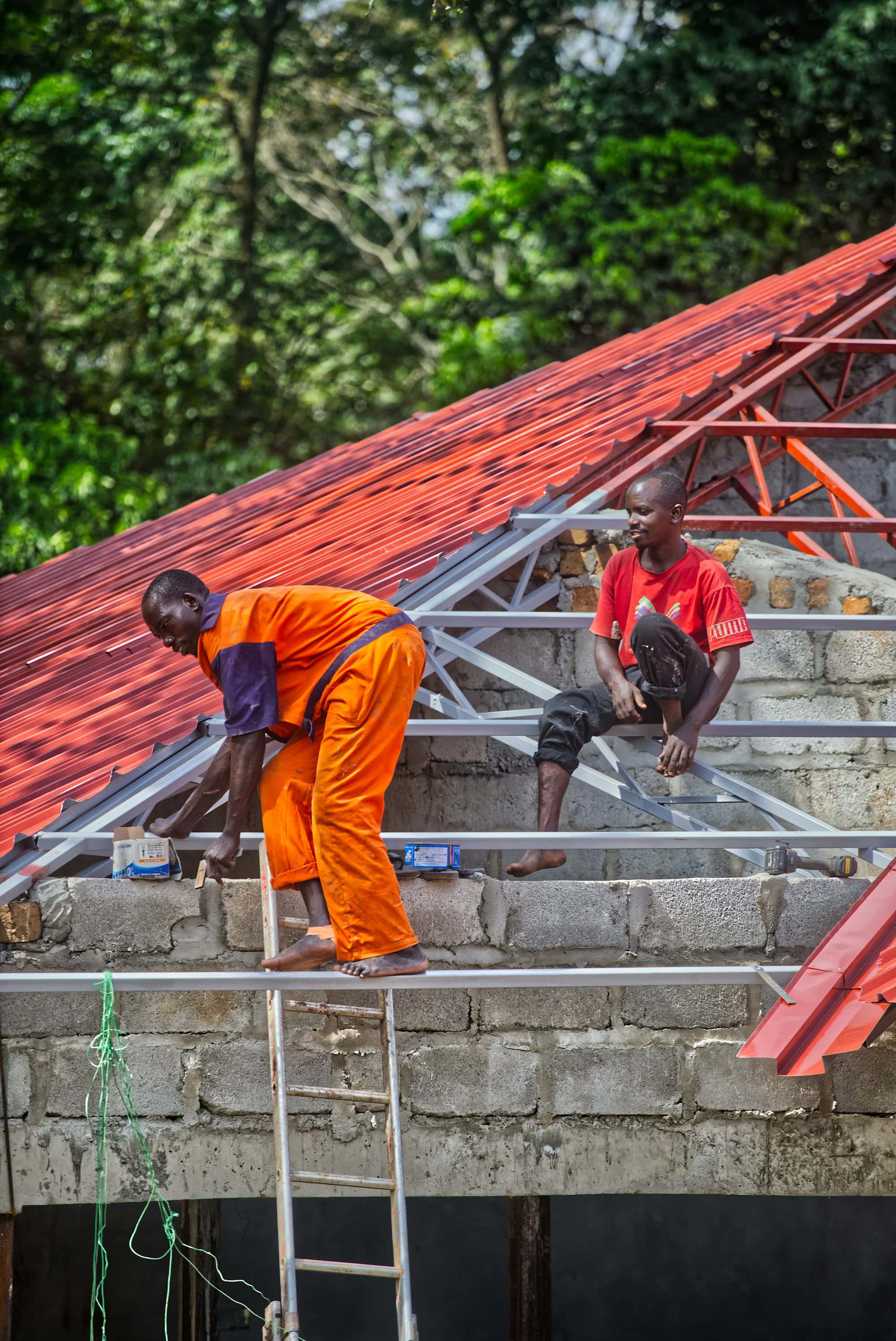 Two roofers working on a roof frame with red metal sheeting