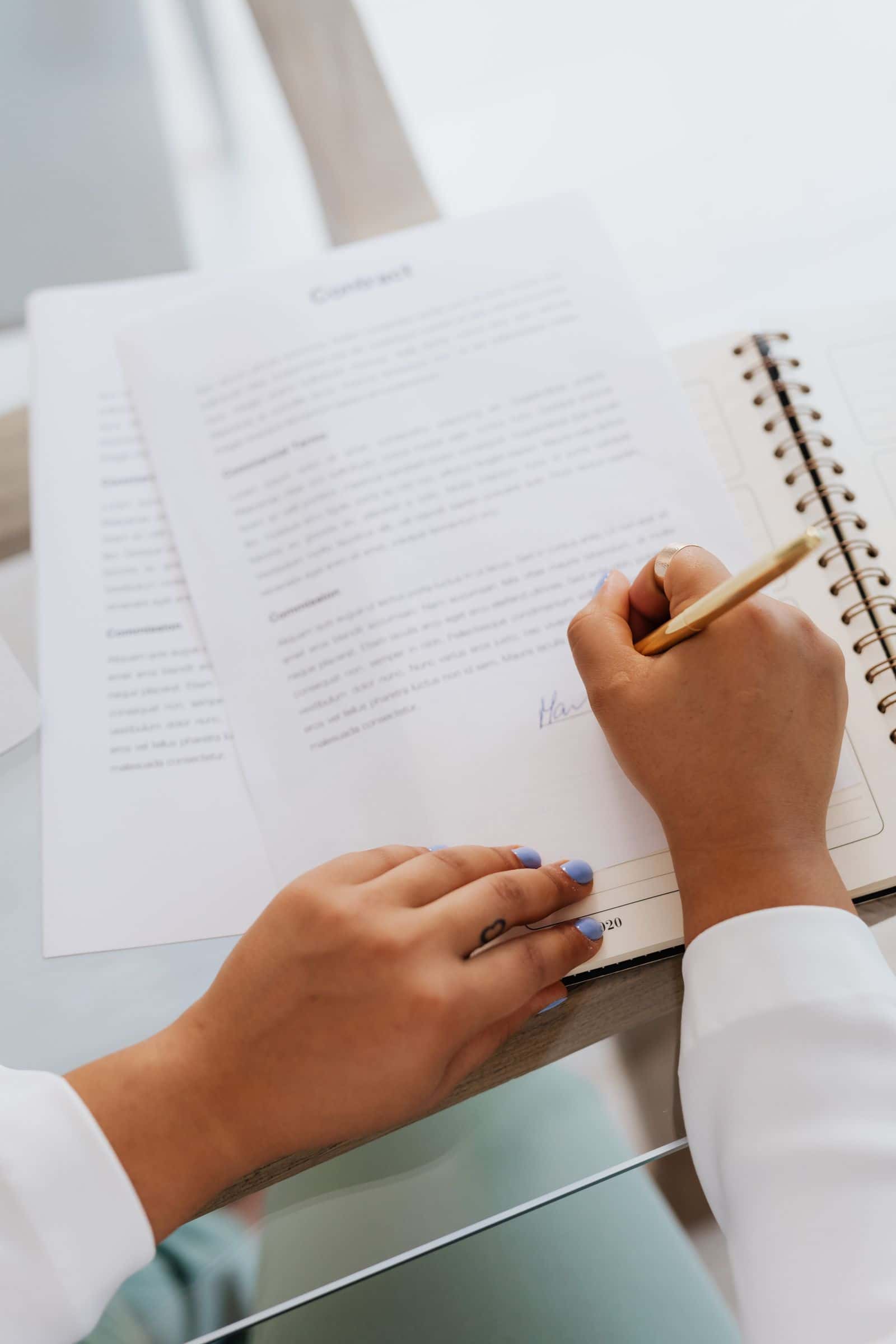 Somebody writing on a notepad next to printed paperwork
