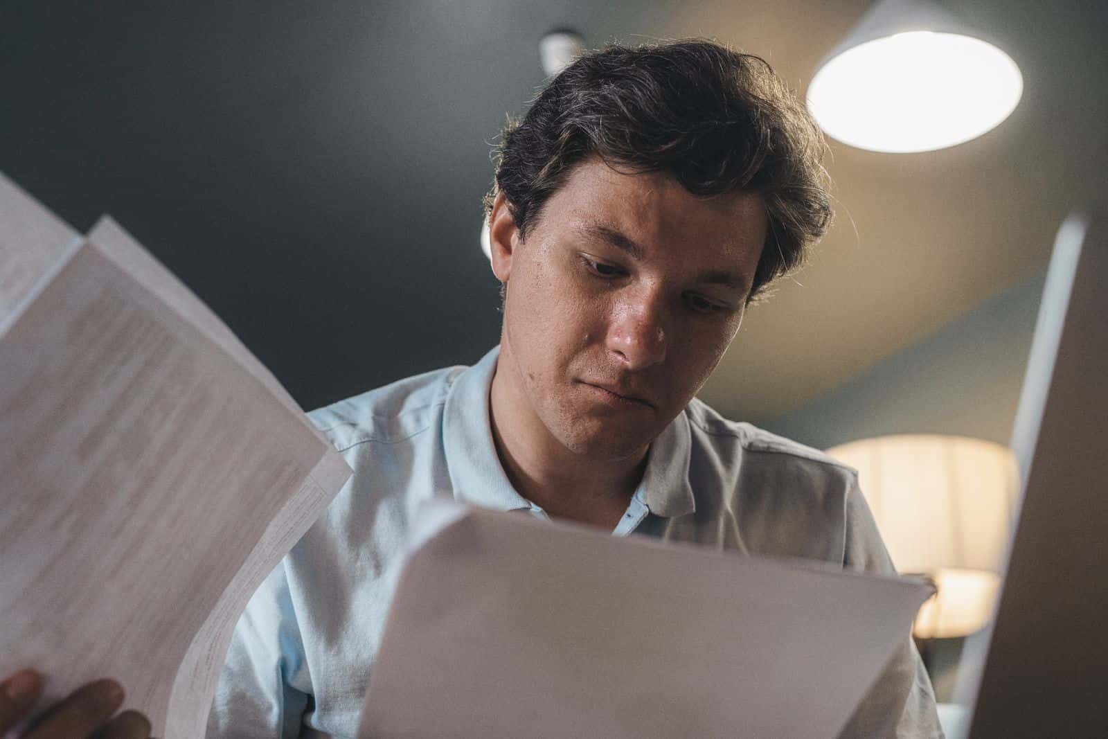 A man reading through a handful of paperwork under a lamp
